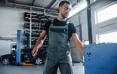 Çekmeceyi açar. Erkek tamirci garajdaki bozuk otomobili tamir etmek için farklı araçlar kullanıyor.