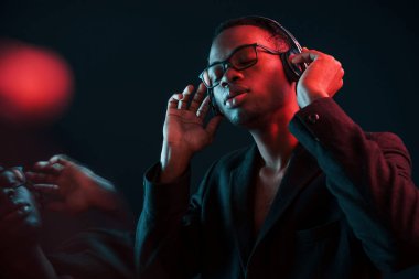 Kulaklıkla müzik dinlemeyi seviyorum. Gözlüklü. Fütürist neon ışıkları. Stüdyodaki Afrikalı Amerikalı genç adam..