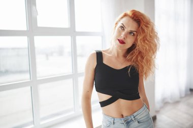 Yukarı bakıyorum. Çekici kızıl saçlı kadın pencerenin yanındaki uzay odasında poz veriyor..