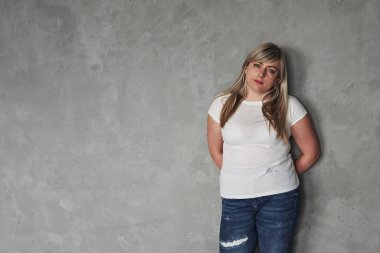 Duvara yaslan. Stüdyodaki genç beyaz kadın gri arka planda duruyor..