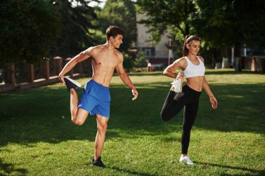 Erkeklerin güzel karın kasları var. Erkek ve kadının şehirde gündüz vakti parkta fitness günü var..