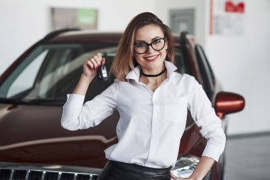 Dost canlısı bayan yönetici otomobil salonunda kırmızı arabaya karşı duruyor.