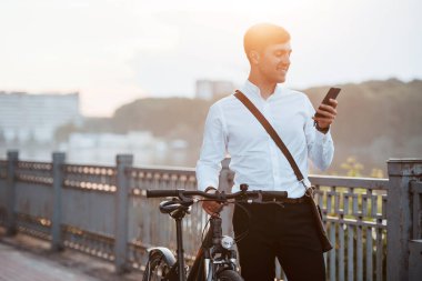 Sosyal medyayı kullanırken gülümsüyor. Siyah bisikletli resmi giysili bir işadamı şehirde..