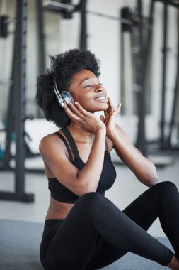 Güzel müzikle tatmin olmak. Kıvırcık saçlı ve spor elbiseli Afrikalı Amerikalı kadın spor salonunda spor yapıyor..