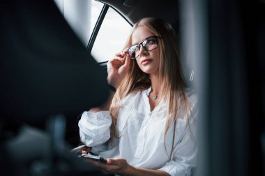 Şoförü beklerken dinleniyor. Zeki iş kadını, siyah iç mekanı olan lüks arabanın arka koltuğunda oturur..