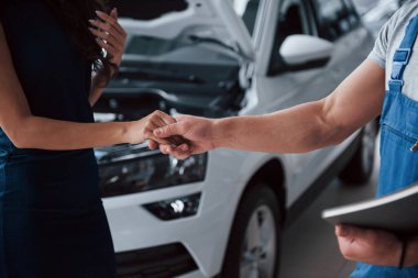 El ele tutuşmak. Otomobil kuaföründe mavi üniformalı bir kadın tamir edilmiş arabasını geri alıyor..