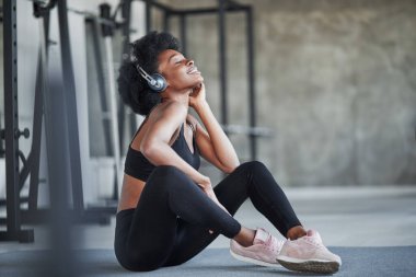 Antrenmandan sonra mola. Kıvırcık saçlı ve spor elbiseli Afrikalı Amerikalı kadın spor salonunda spor yapıyor..