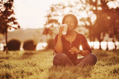 Taze kahve içiyorum. Yazın parktaki neşeli Afrikalı Amerikalı kadın..