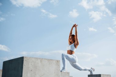 Çimento küpünün üzerinde duruyor. Spor yapan bir kadının gündüz vakti göl kenarında spor egzersizleri yapması..