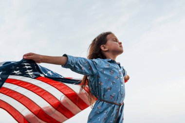 Amerikan Bayrağı elinde olan vatansever kadın çocuk. Bulutlu gökyüzüne karşı.