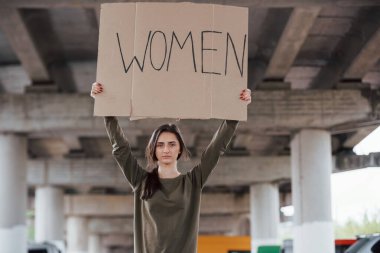 Tek başınasın. Ellerinde el yapımı feminist posteriyle gündelik giysiler içinde güzel bir kız..