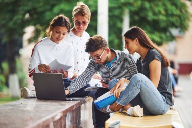 İşine odaklan. Dizüstü bilgisayarla. Gündüz vakti şehirde günlük kıyafetler giyen bir grup genç öğrenci..