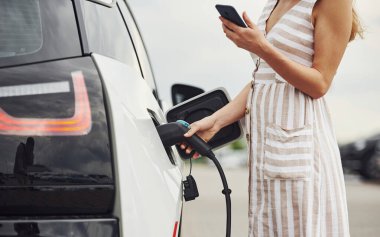 Elektrikli arabalardaki kadın gündüz şarj istasyonunda. Yepyeni bir araç..