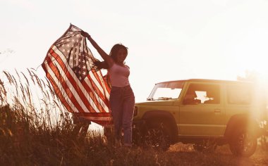 Kız öne doğru koşuyor. Arkadaşlarının hafta sonları açık havada yeşil arabalarının yanında Amerikan bayrağı taşıyorlar..