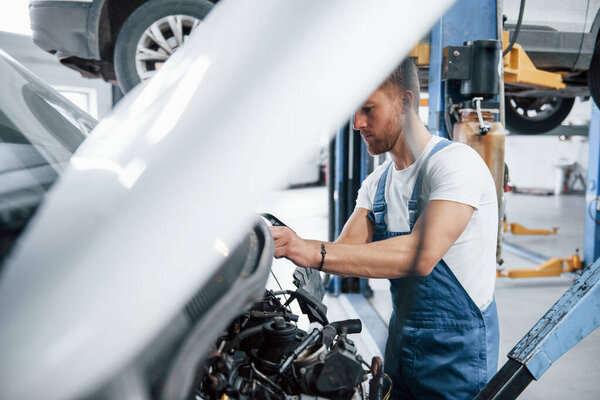 Hood is up. Employee in the blue colored uniform works in the automobile salon.