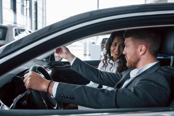 Active conversation. Lovely successful couple trying new car in the automobile salon.