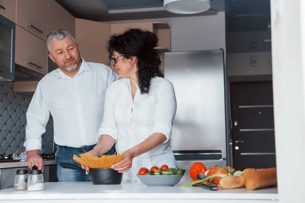 古いが幸せだ 台所で野菜を使った料理を作る白いシャツを着た男と妻 — ストック写真