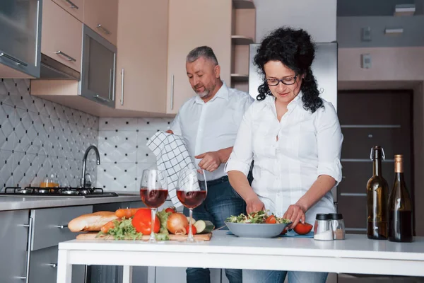 タオルを手に 台所で野菜を使った料理を作る白いシャツを着た男と妻 — ストック写真