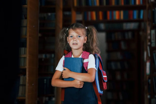 Χαριτωμένο Κοριτσάκι Σακίδιο Στέκεται Στη Βιβλιοθήκη Γεμάτη Βιβλία Σύλληψη Της — Φωτογραφία Αρχείου