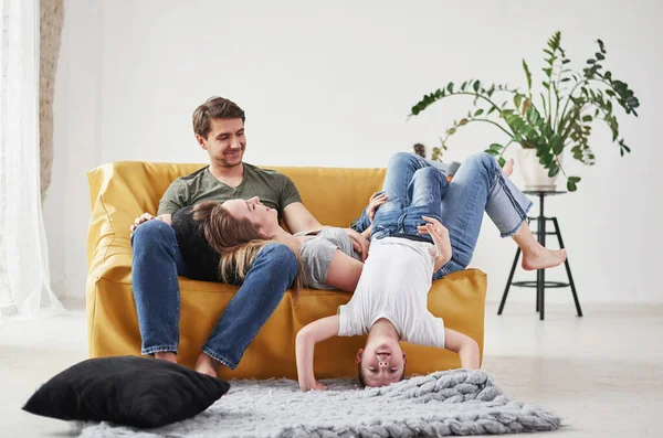 子供はバカよ 幸せな家族は彼らの新しい家のリビングルームの黄色のソファで楽しみを持っています — ストック写真