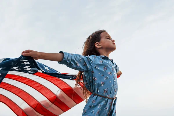 Amerikan Bayrağı elinde olan vatansever kadın çocuk. Bulutlu gökyüzüne karşı.