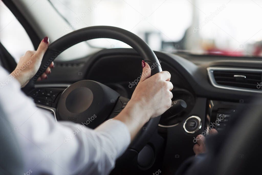 Hands on steering wheel. Woman in official clothes trying her new car in automobile salon.