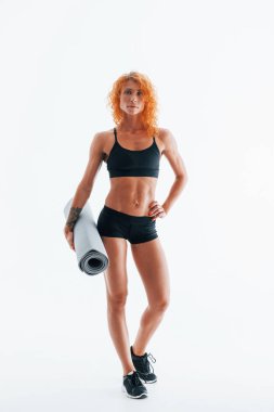 Gri renkli paspası elinde tutuyor. Kızıl saçlı kadın vücut geliştirici beyaz arka planda stüdyoda..