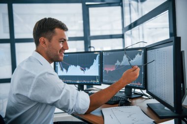 İşine odaklan. Resmi giyinmiş genç iş adamı birden fazla ekranla ofiste. Değişim ve para kavramı.