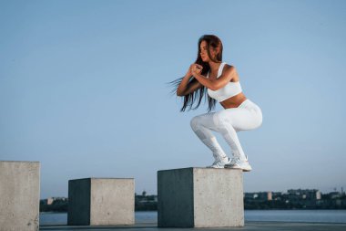 Çimento küpüne çömelmek. Spor yapan bir kadının gündüz vakti göl kenarında spor egzersizleri yapması..