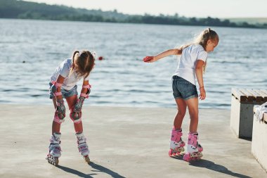 İki çocuk gündüz vakti göl kenarında paten sürmeyi öğreniyor..
