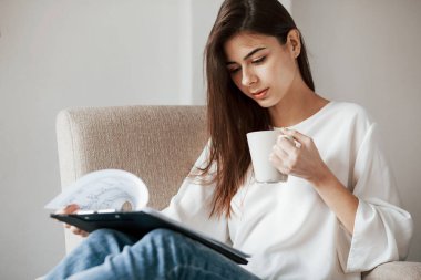 Plana odaklan. Beyaz duvarları ve pencereden gelen gün ışığıyla odada genç bir esmer..