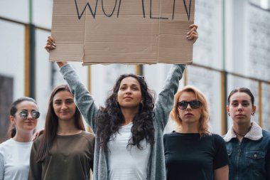 Elinde bir tabelayla. Bir grup feminist kadın dışarıda hakları için protesto yapıyor..