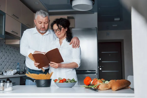 興味深い情報だ 台所で野菜を使った料理を作る白いシャツを着た男と妻 — ストック写真