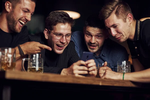 智能手机上有趣的内容 三个朋友手里拿着啤酒在酒吧休息 谈话时 — 图库照片