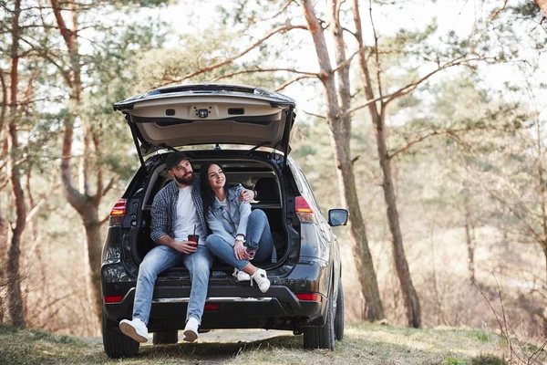 田舎の風景 車の後部に座っている 自然を楽しむ 夫婦は彼らのブランドの新しい黒い車で森に到着しました — ストック写真
