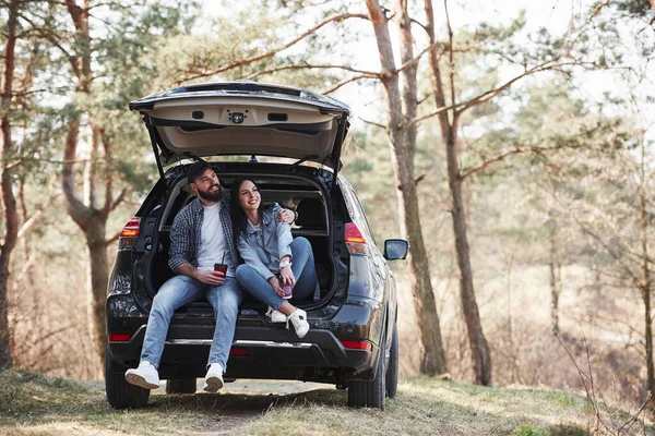 二人だけだ 車の後部に座っている 自然を楽しむ 夫婦は彼らのブランドの新しい黒い車で森に到着しました — ストック写真