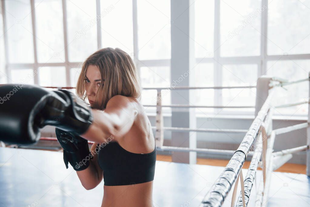 Fast move. Female sportswoman training in the boxing ring. In black colored clothes.