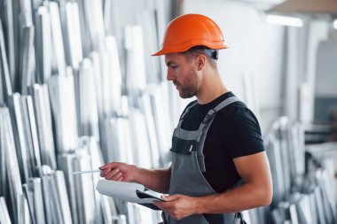 Depodaki nesneleri saymak ve kontrol etmek. Fabrikada sanayi işçisi. Turuncu şapkalı genç teknisyen..