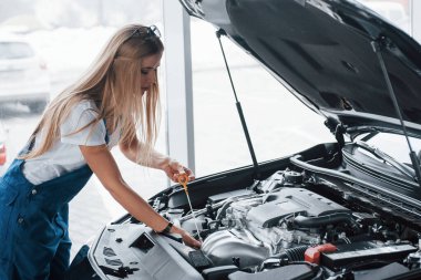 Tamamen işe odaklanmış. Güzel bir iş için. Araba bağımlısı kadın siyah otomobili kapalı alanda tamir ediyor..