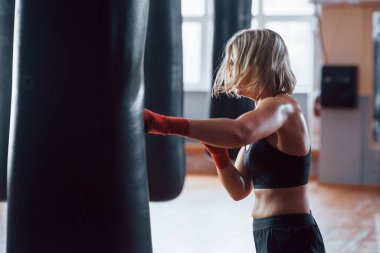 Tam komisyon. Dişi boksör torbayı yumrukluyor. Sarışın spor salonunda egzersiz yapıyor..