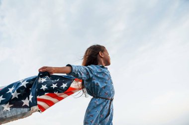 Amerikan Bayrağı elinde olan vatansever kadın çocuk. Bulutlu gökyüzüne karşı.