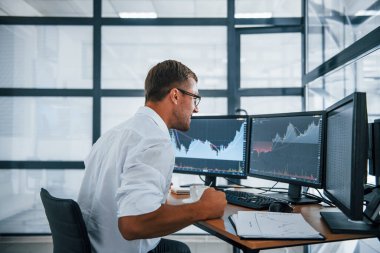 Heyecanlı ve mutlu. Zafer ve başarı kavramı. Resmi giyinmiş genç işadamı birden fazla ekranla ofiste..