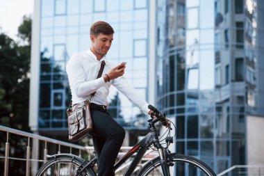 Kahverengi çanta ve pembe telefon. Siyah bisikletli resmi giysili bir işadamı şehirde..