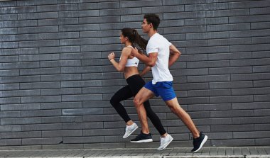 Sağlıklı bir yaşam tarzı. Erkek ve kadının fitness günü ve şehirde gündüz vakti tuğla duvarın yanında koşuyorlar..