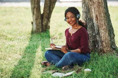 Çimlerin üzerinde oturuyor. Yazın parktaki neşeli Afrikalı Amerikalı kadın..