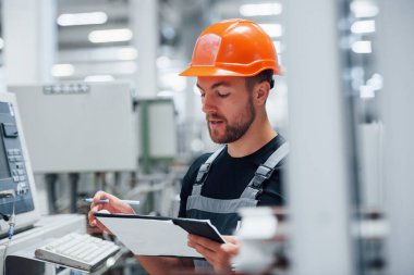 Not alıyorum. Fabrikada sanayi işçisi. Turuncu şapkalı genç teknisyen..