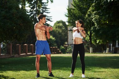 Erkeklerin güzel karın kasları var. Erkek ve kadının şehirde gündüz vakti parkta fitness günü var..