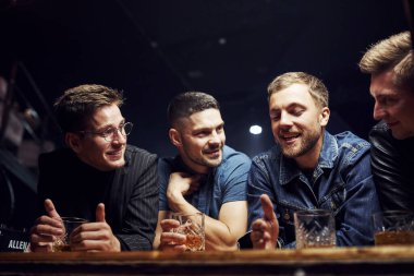 Ön manzara. Arkadaşlar ellerinde alkolle barda dinleniyorlar. Sohbet ederken.