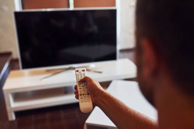 İnsanın arka görünümü uzaktan kumandayı elinde tutuyor ve televizyonu açıyor.