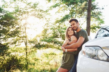 Beyaz arabanın ön tarafında. Genç ve güzel bir çift gündüz vakti ormanda iyi vakit geçirir..